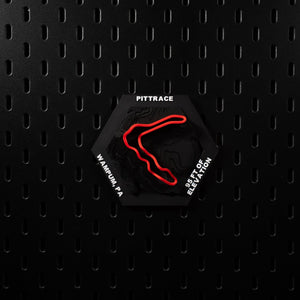PittRace hex square to camera on a black pegboard wall, red loop lit against deep shadow