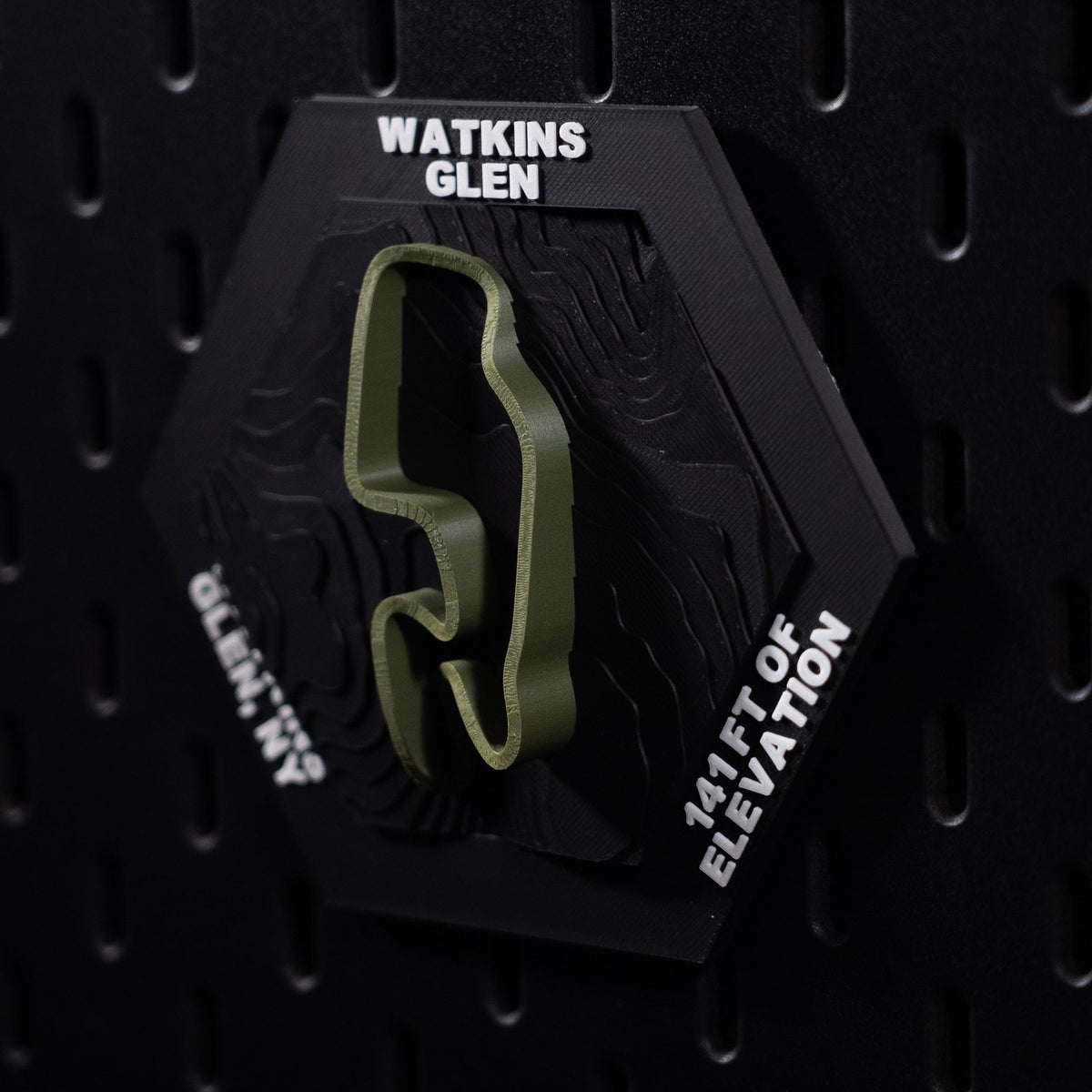 Watkins Glen hex three quarter view, the whole olive lap sharp against black pegboard