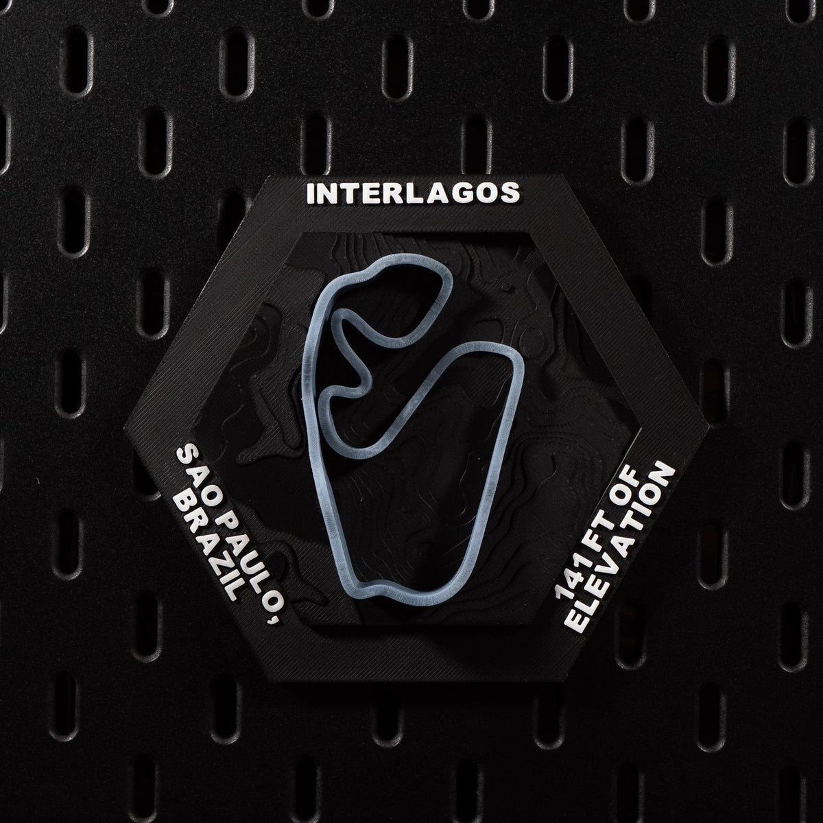Interlagos hex flat on black pegboard, pale blue track loop set into dark contour terrain
