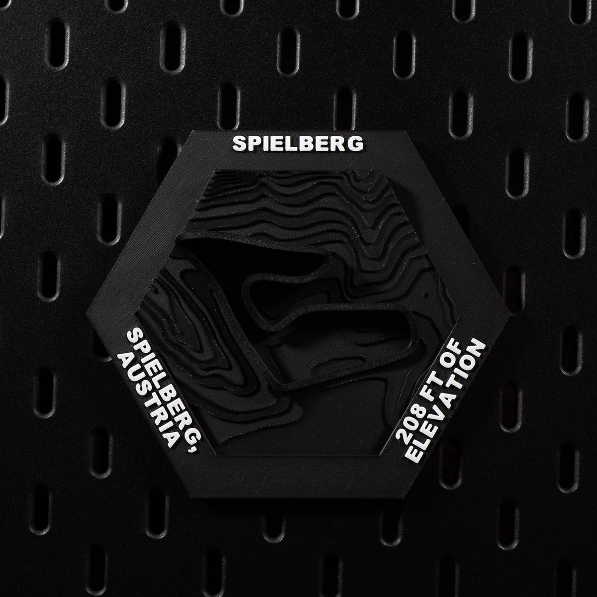 Spielberg hex flat on black pegboard, black on black with the circuit cut into terraced terrain